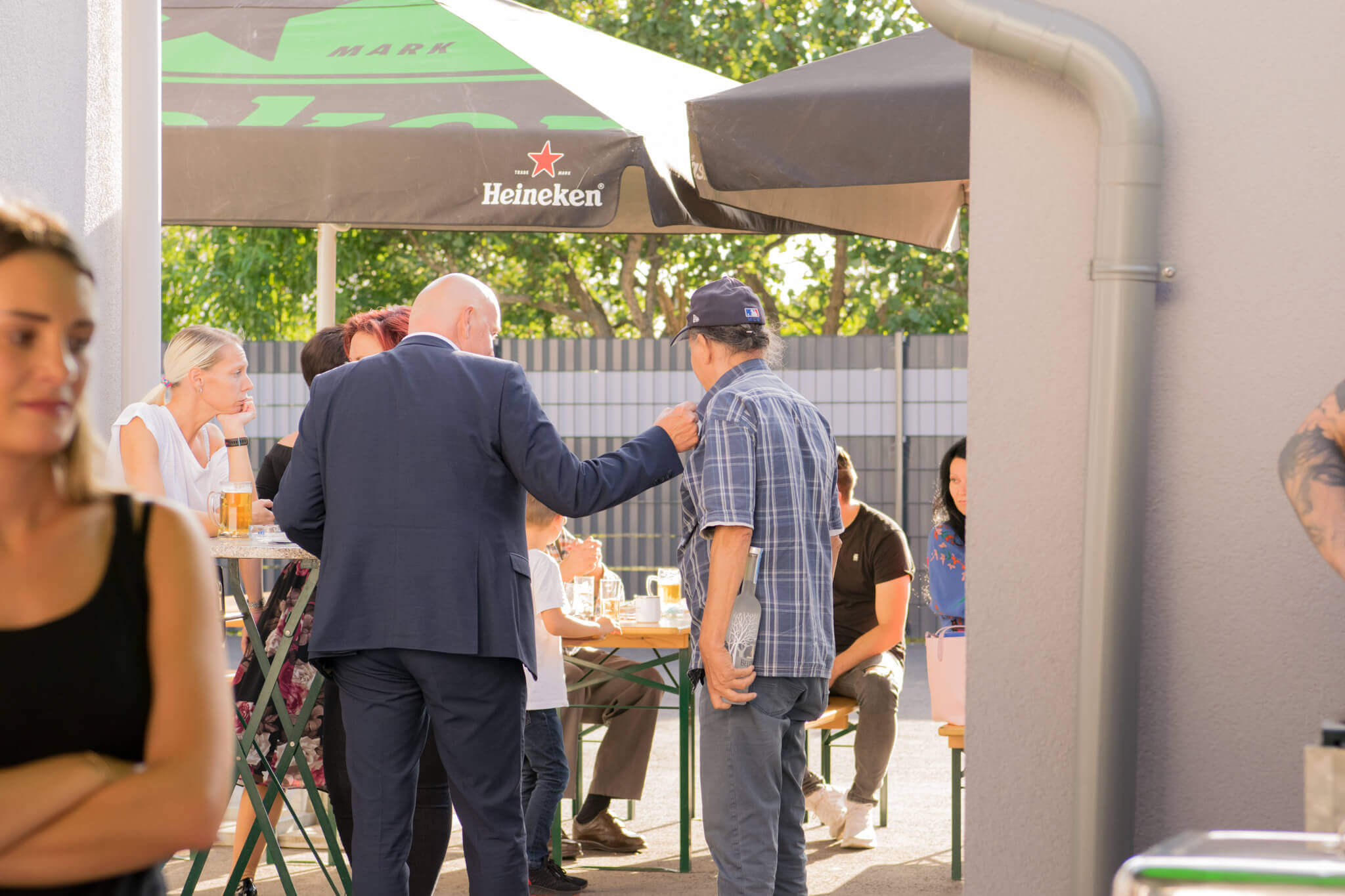 Gesellige Runde im Biergarten bei sonnigem Wetter, Menschen plaudern an Biertischen mit Heineken-Schirm.