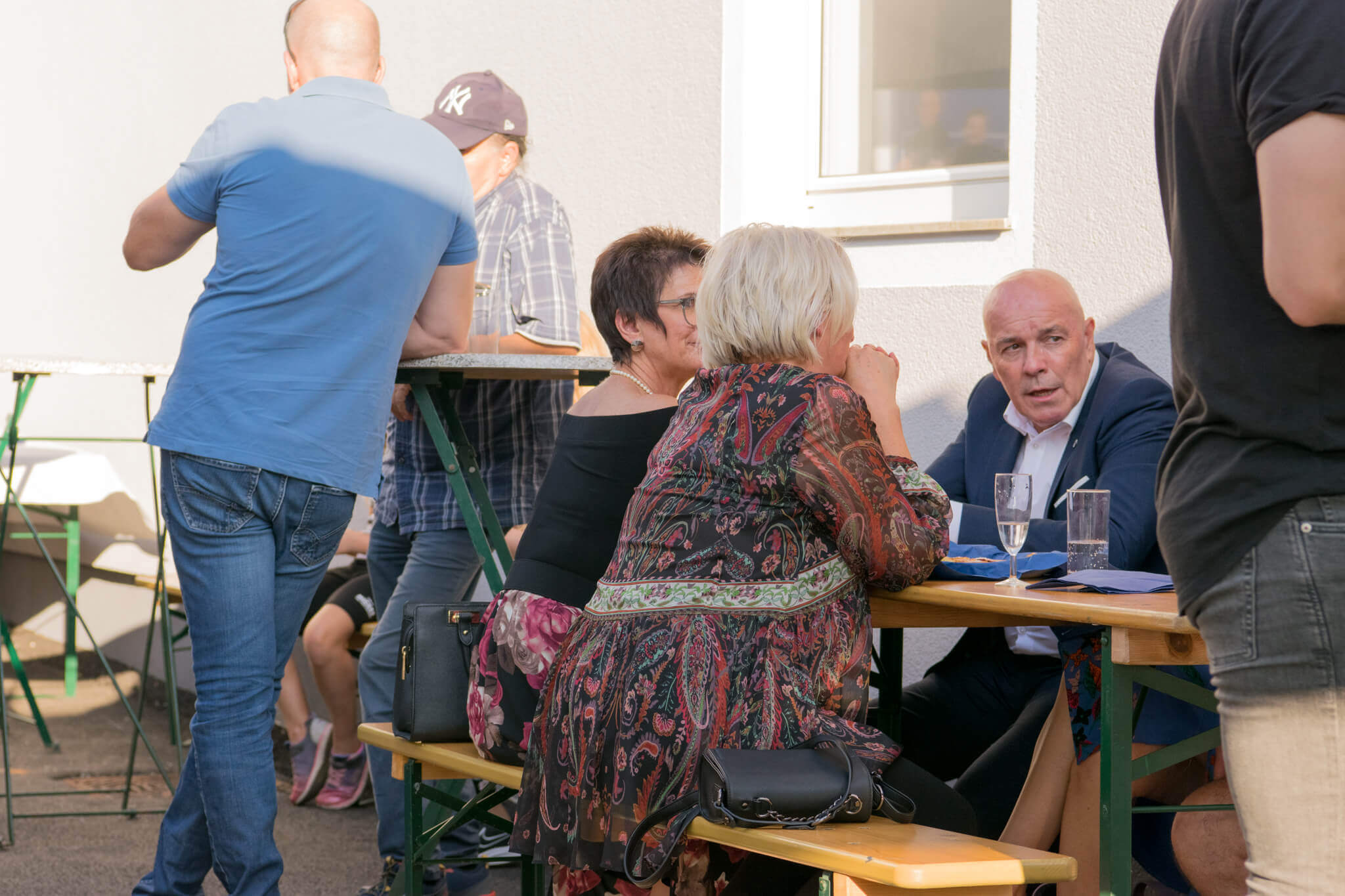 Gruppe von Menschen unterhält sich lebhaft an einem Tisch im Freien bei Sonnenschein.