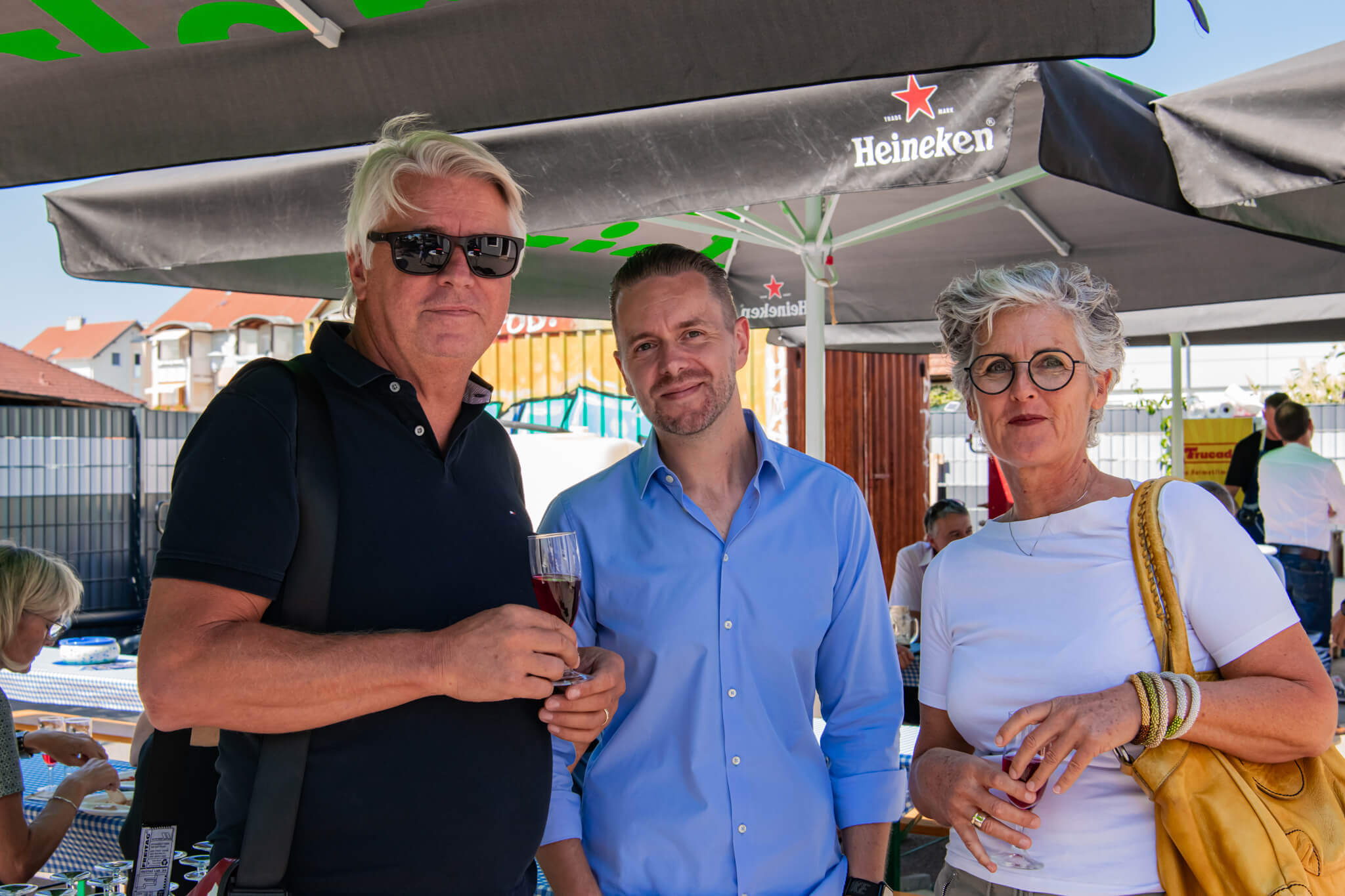 Drei Personen genießen ein Sommerfest im Freien unter einem Heineken-Schirm, trinken und unterhalten sich.