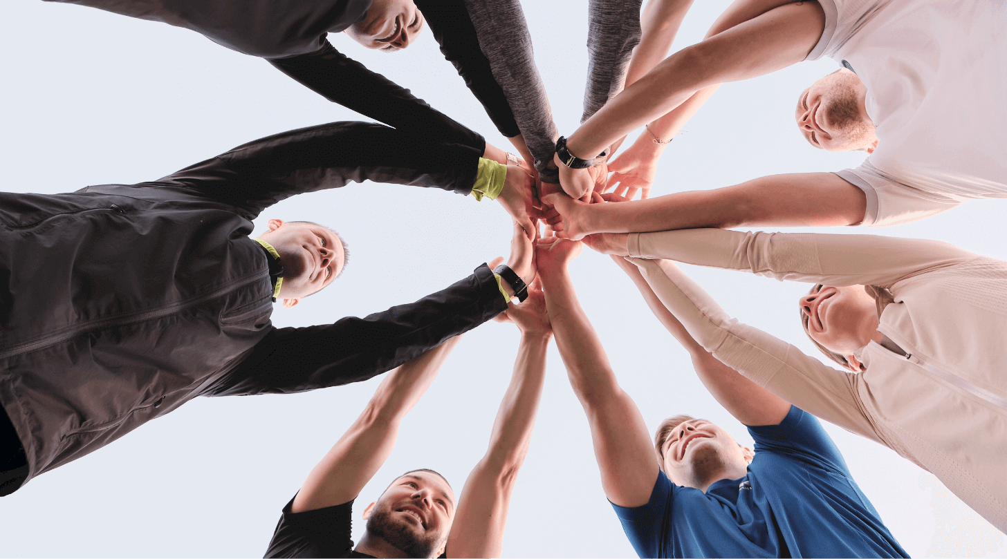 Gruppe von Menschen bildet einen Handschlag-Kreis zur Förderung von Teamgeist und Zusammenarbeit im Freien.
