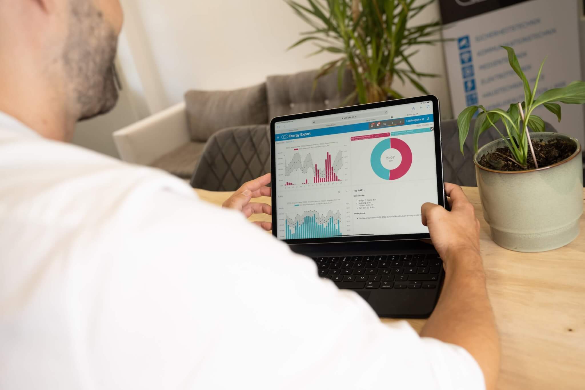 Mann analysiert Diagramme und Statistiken auf einem Laptop am Tisch, neben einer Pflanze.