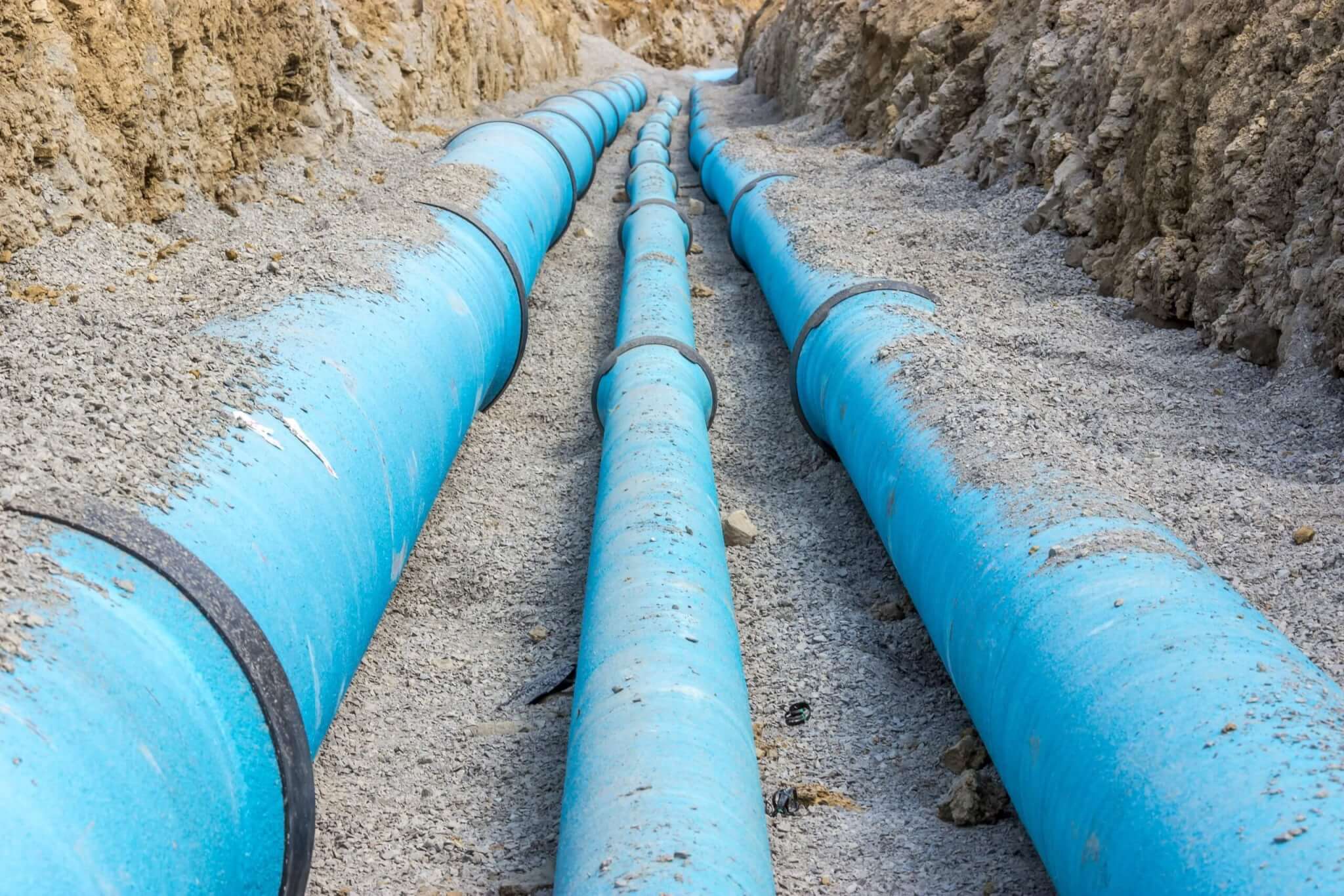 Blaue Wasserrohre im Erdgraben, bereit für den Anschluss an die städtische Wasserversorgung.
