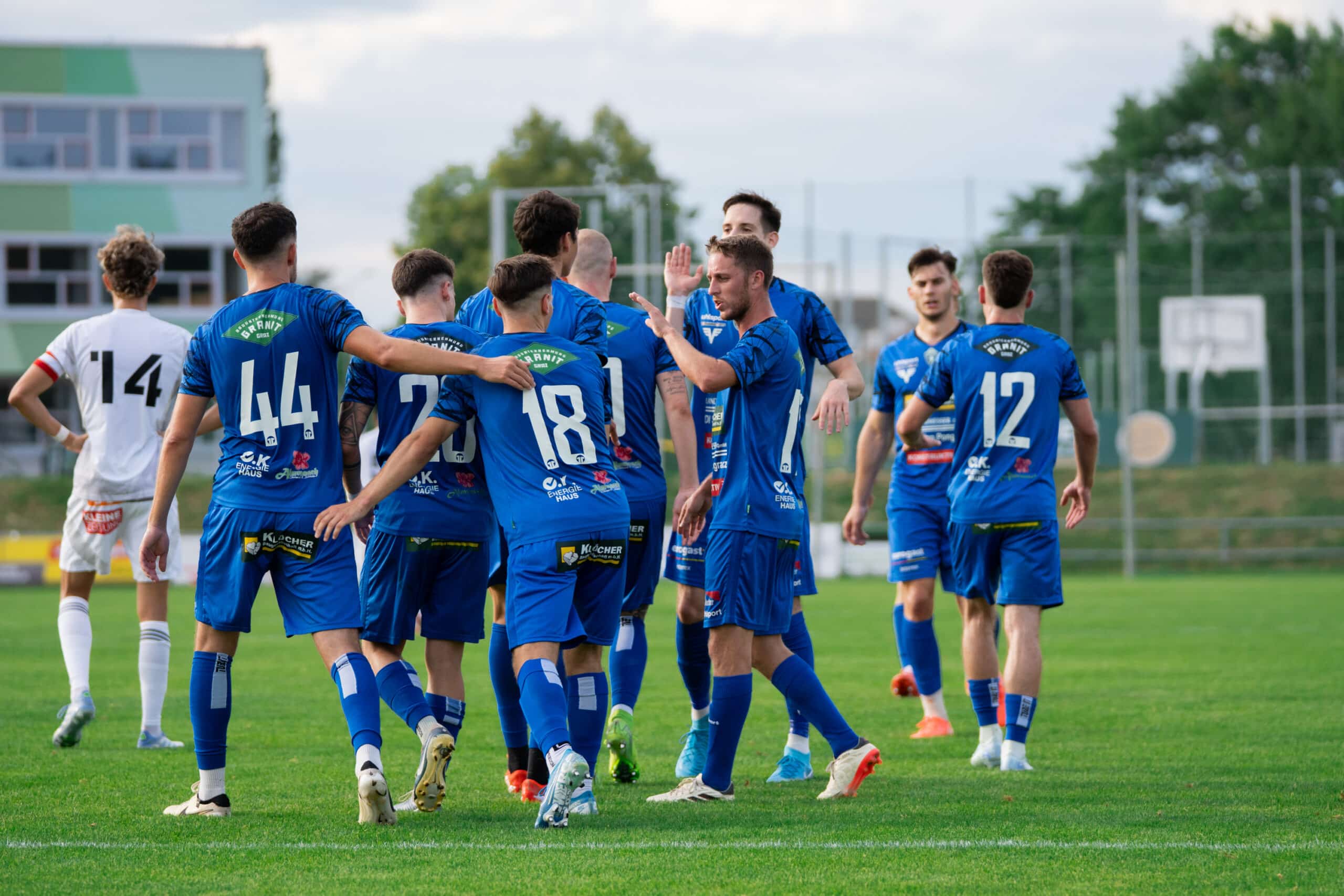 Fußballspieler in blauen Trikots feiern ein Tor auf dem Spielfeld bei einem spannenden Match im Freien.