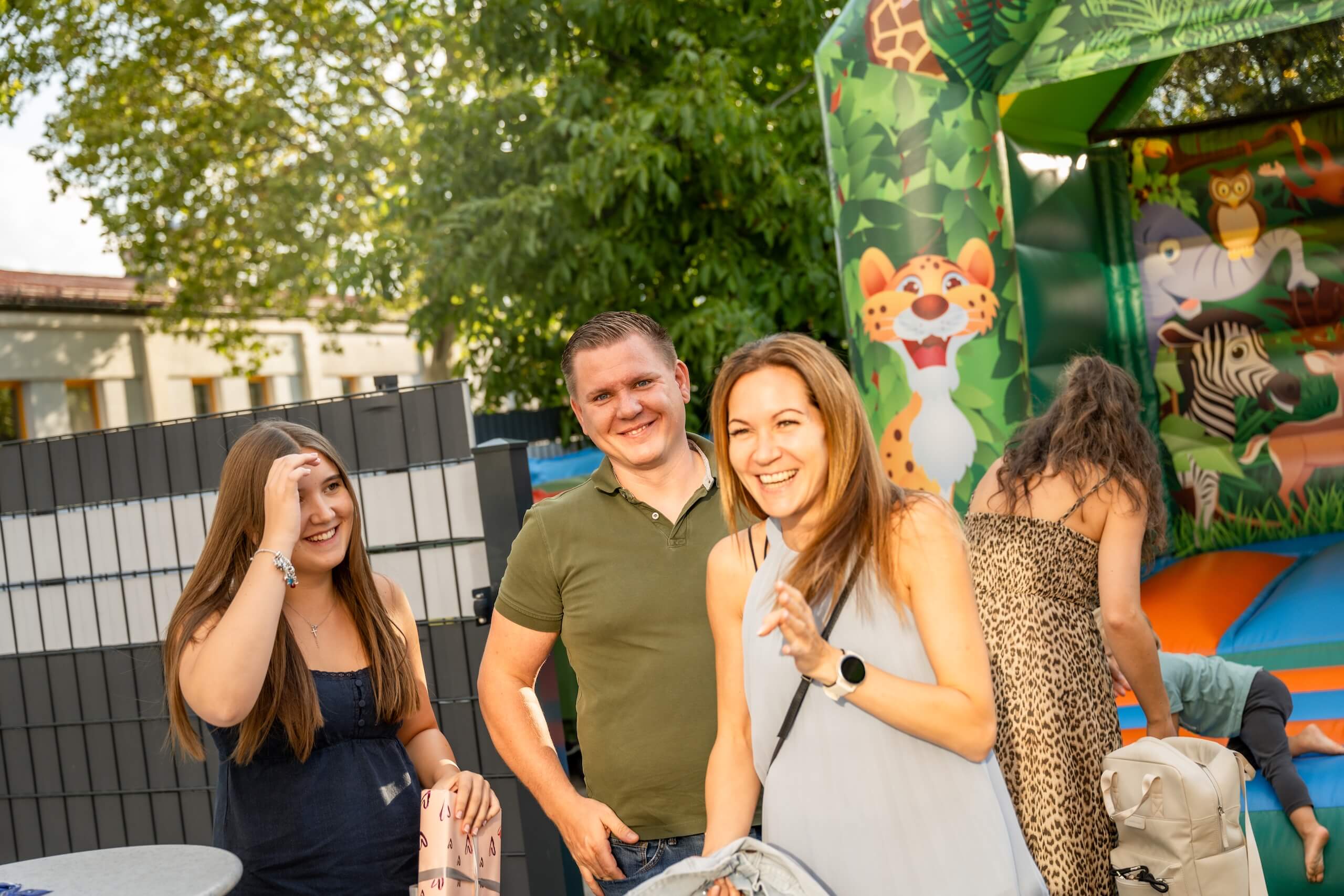 Fröhliche Menschen bei einer Sommerparty im Freien mit Hüpfburg im Hintergrund.