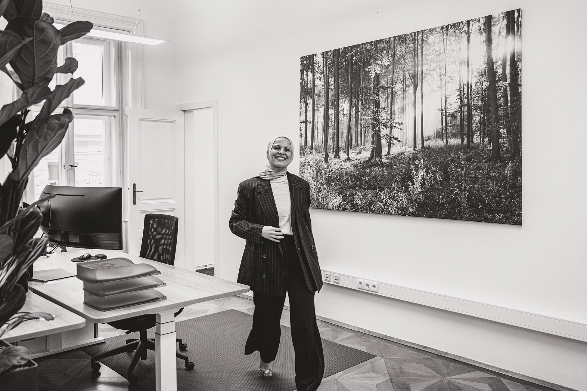 Eine Person lächelt im modernen Büro der Webschmiede, umgeben von Pflanzen und einem großen Waldfoto an der Wand.