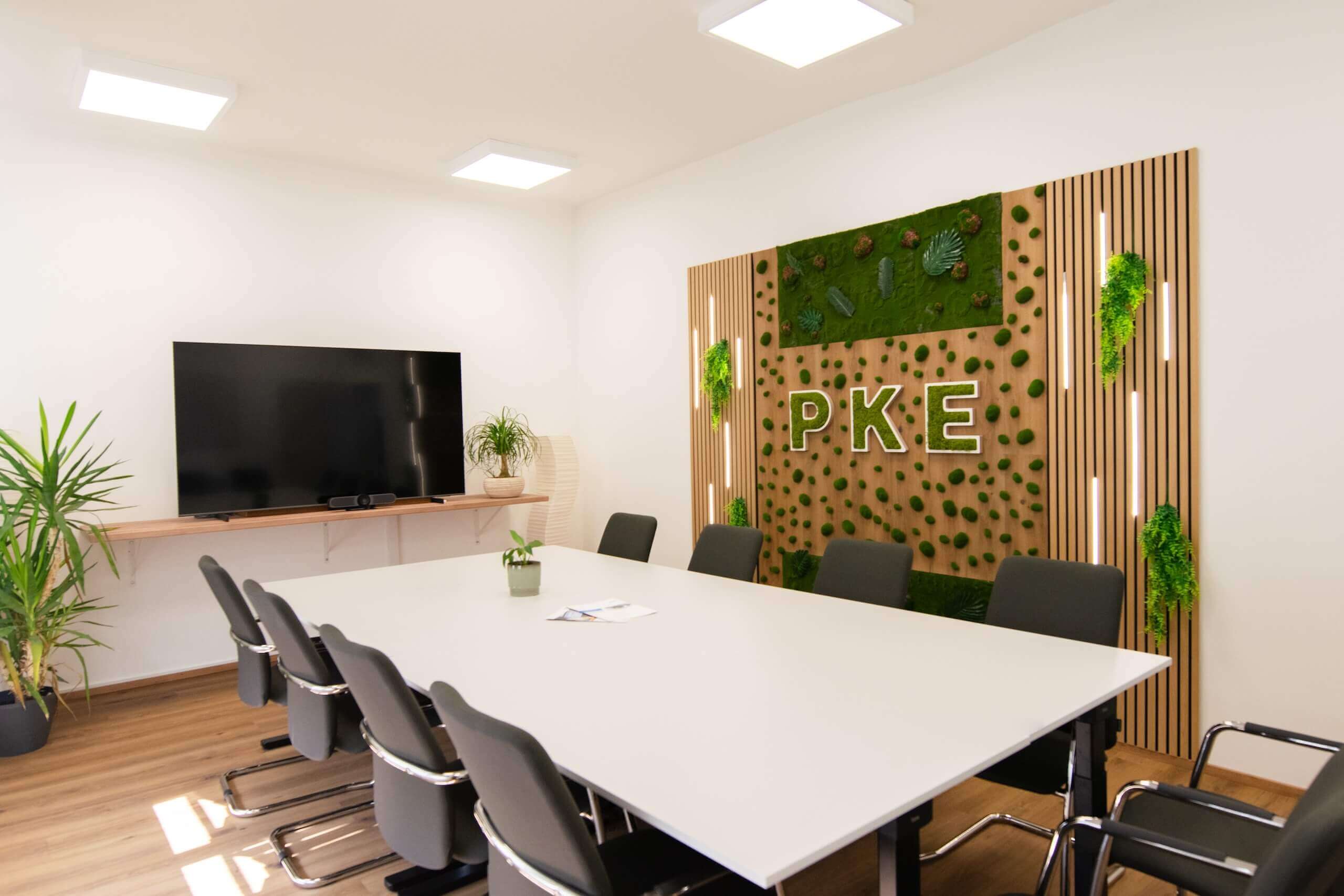 Moderner Konferenzraum bei Webschmiede mit großem Bildschirm, Pflanzen und PKE-Logo an der begrünten Wand.
