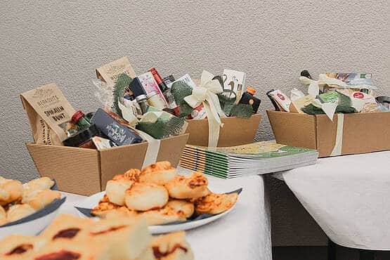 Geschenkkörbe auf dem Tisch, gefüllt mit Delikatessen und Geschenken, daneben Teller mit Gebäck und Broschüren.