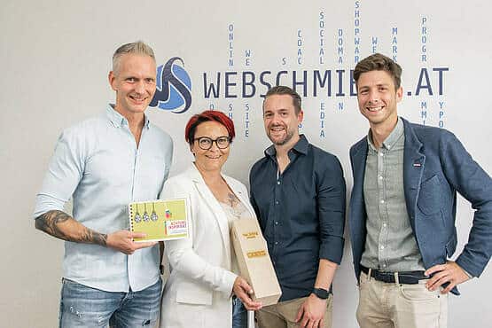 Vier Teammitglieder der Webschmiede Agentur posieren lächelnd vor dem Firmenlogo und halten Auszeichnungen in den Händen.