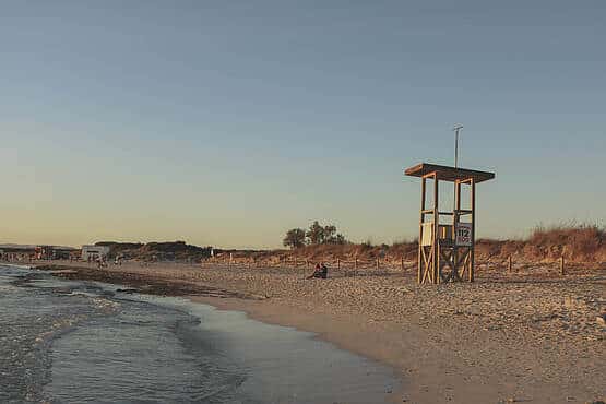 Strand bei Sonnenuntergang mit Rettungsturm, sandige Dünen und ruhiges Meer im Hintergrund.
