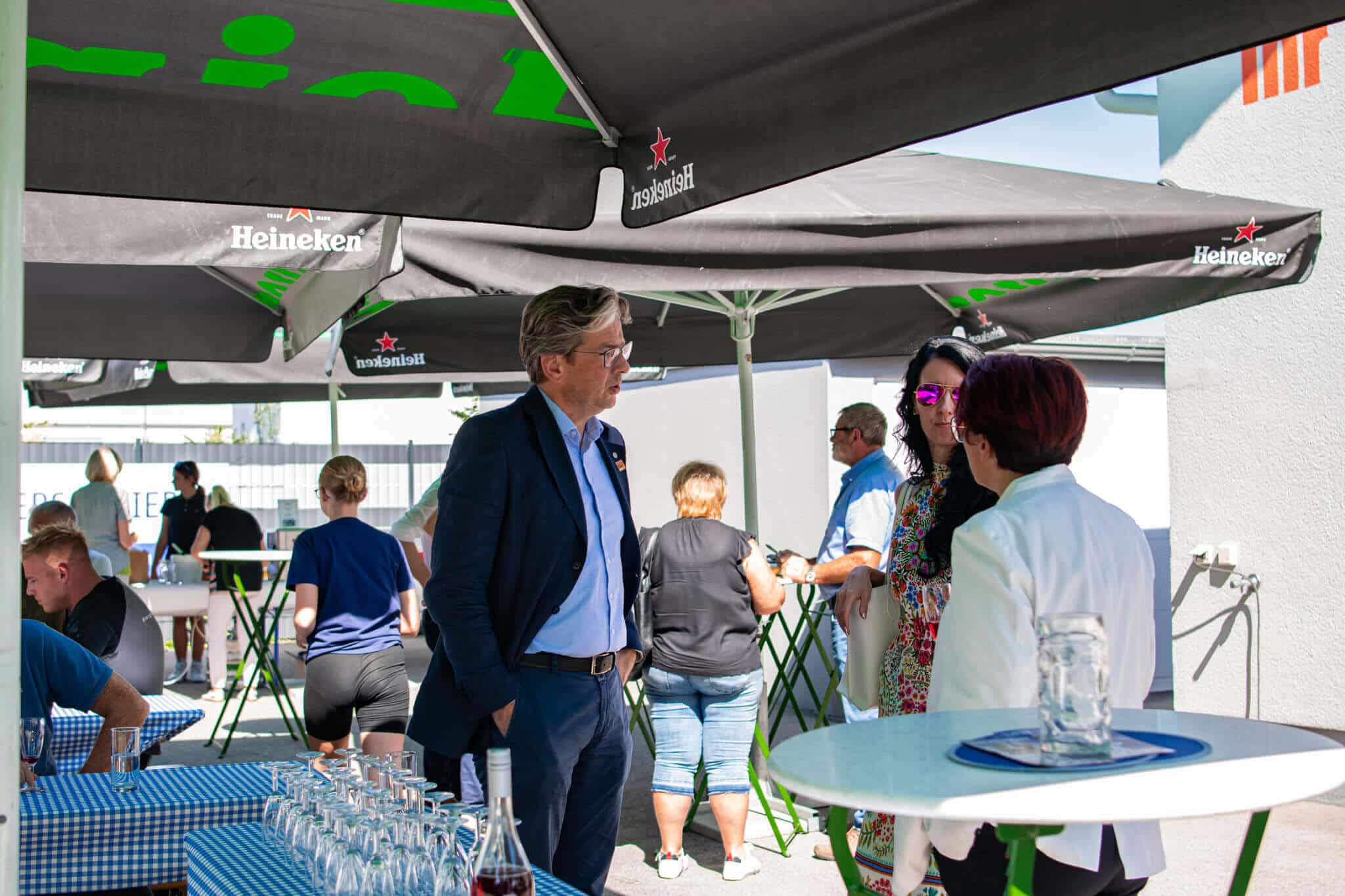 Menschen unterhalten sich auf einer Außenterrasse mit Heineken-Sonnenschirmen bei einer Veranstaltung.