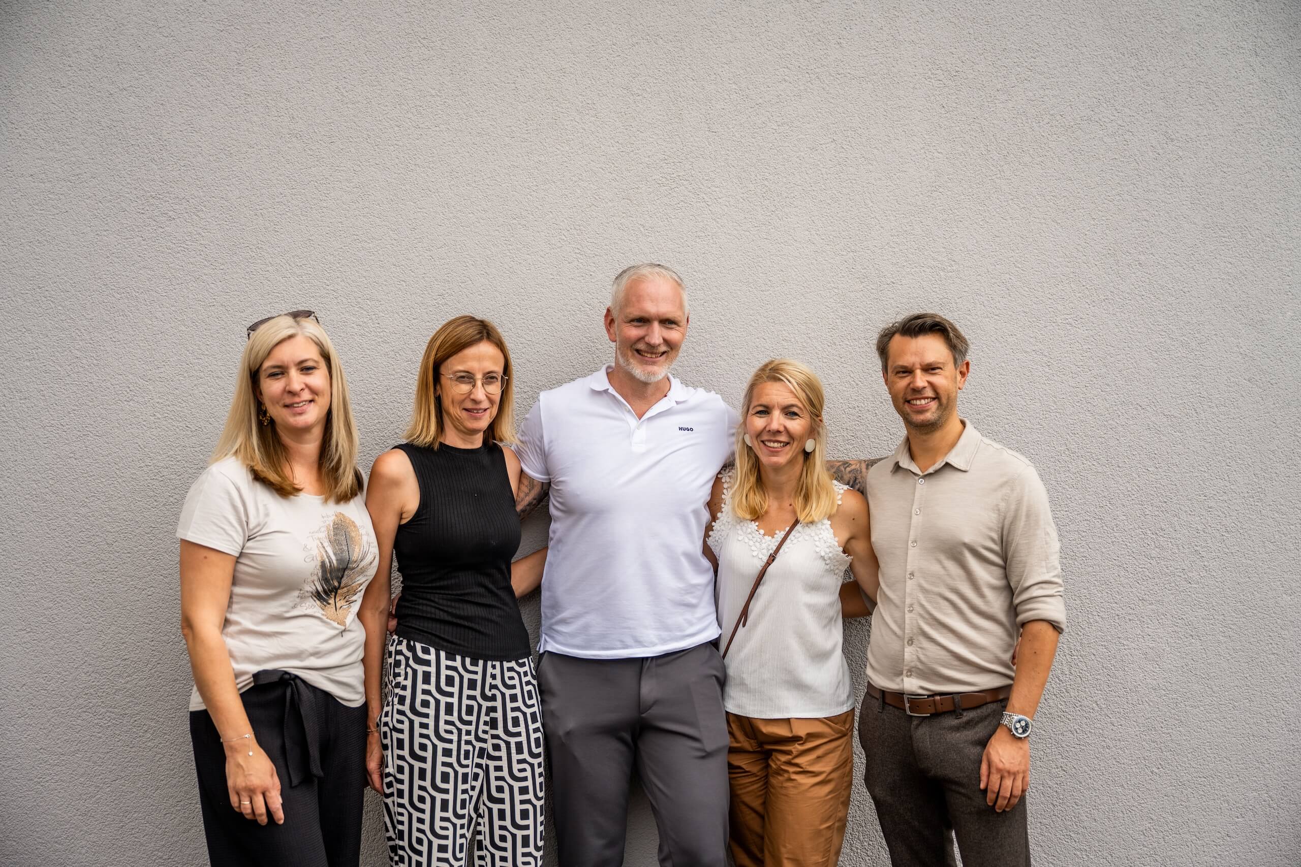 Team der Webschmiede Agentur in Oberwart steht lächelnd vor einer Wand.