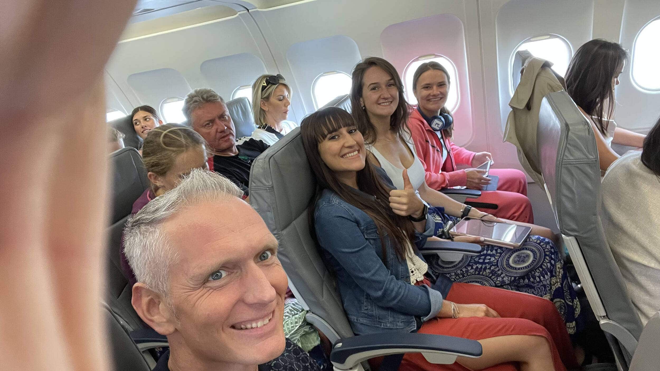 Personengruppe lächelt im Flugzeug, sitzend in einer Reihe, entspannte Atmosphäre.