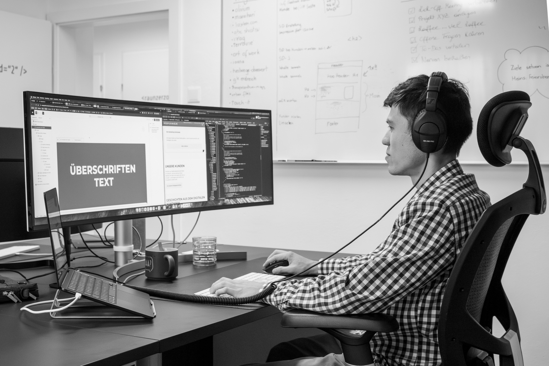 Mitarbeiter der Webschmiede arbeitet konzentriert mit Headset an WordPress-Design auf großem Monitor im Büro.