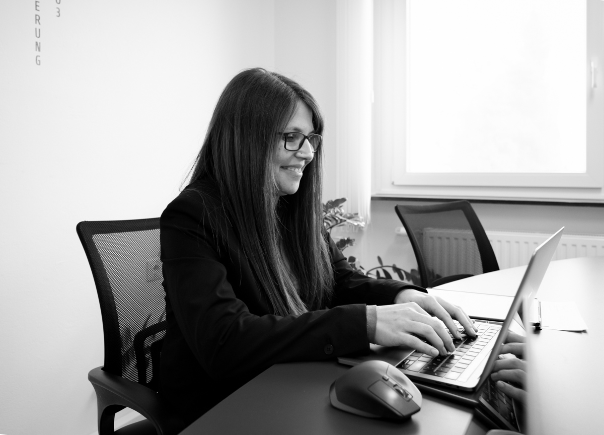 Mitarbeiterin der Webschmiede Agentur arbeitet lächelnd an einem Laptop im Büro, fokussiert auf Webdesign und SEO.