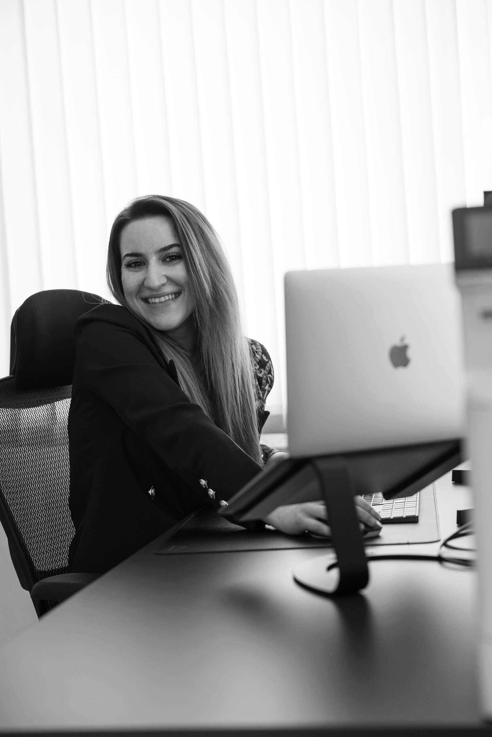 Eine Mitarbeiterin der Webschmiede arbeitet lächelnd an einem Laptop in einem modernen Büro.