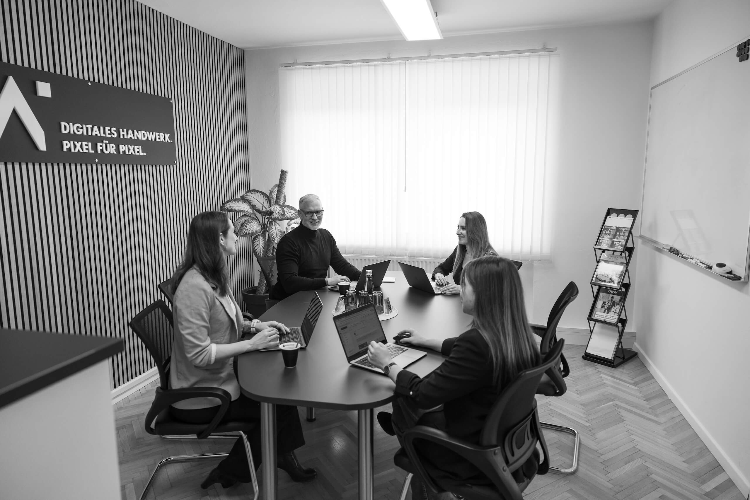 Team in Besprechung am Konferenztisch mit Laptops, im Büro der Webschmiede, WordPress Agentur Oberwart.