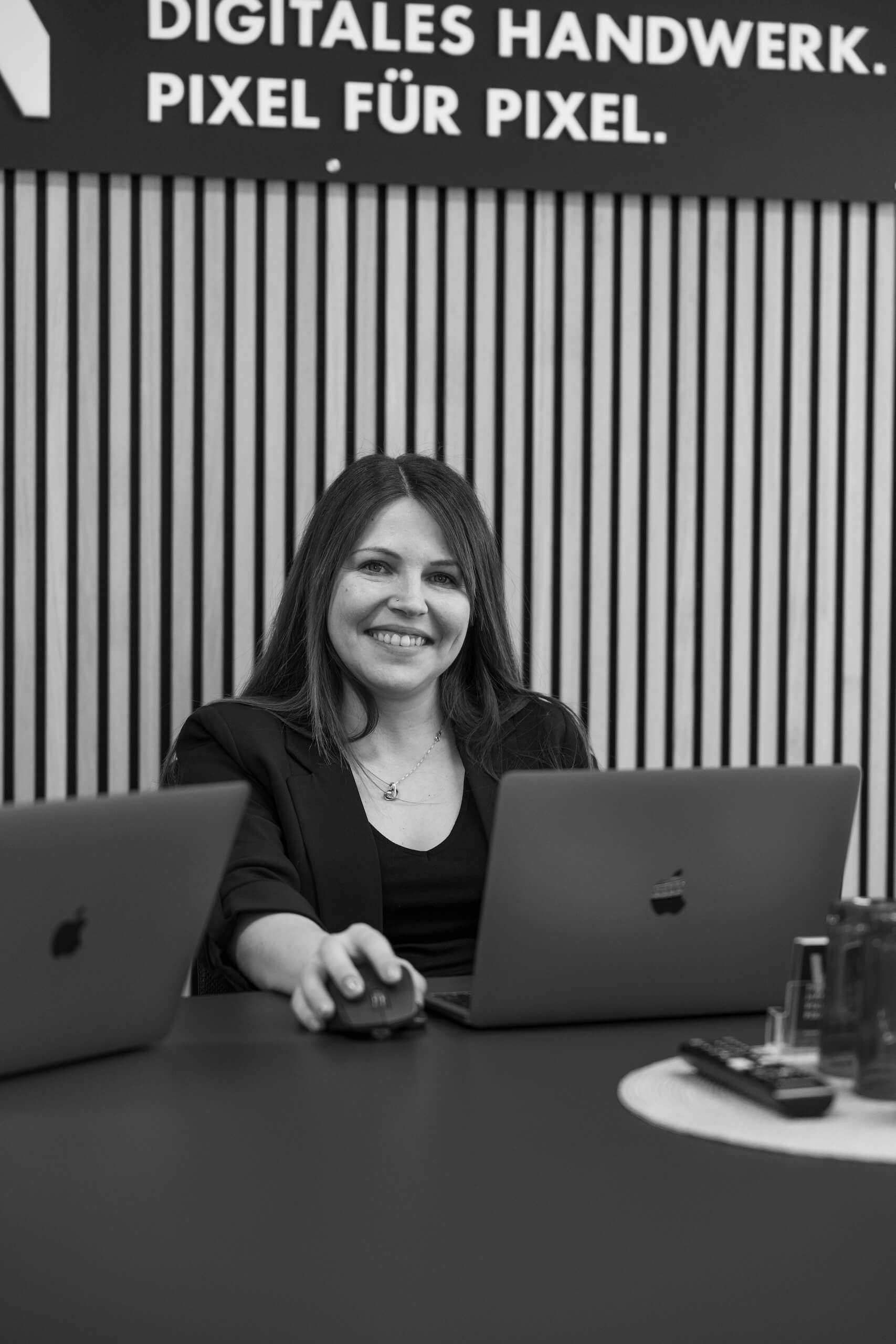 Mitarbeiterin der Webschmiede sitzt lächelnd am Laptop, arbeitet an einem WordPress-Projekt im modernen Büro.