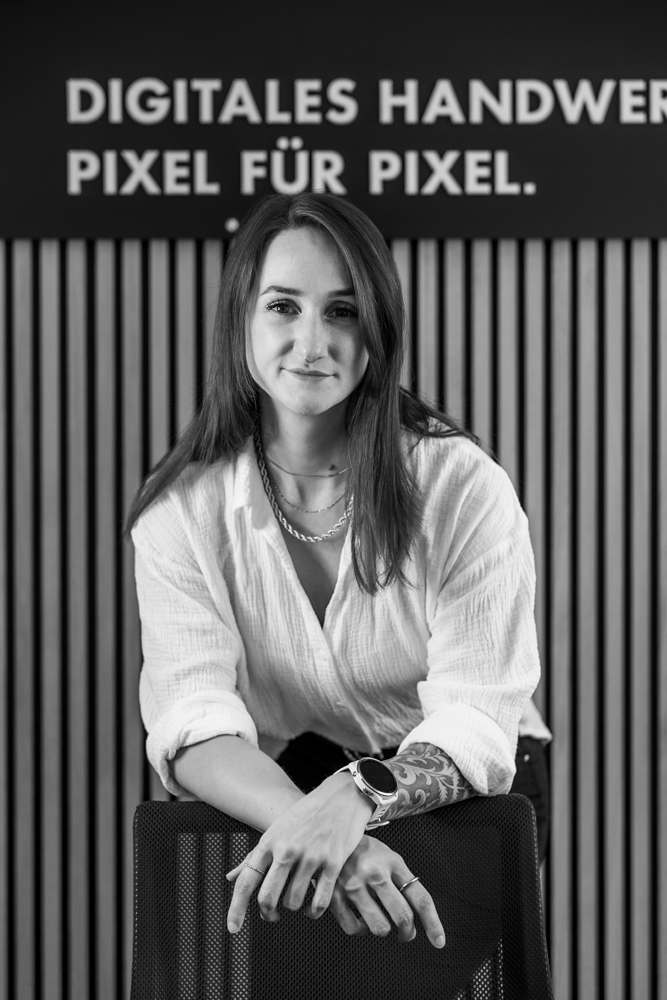 Mitarbeiterin der WordPress Agentur vor einem Schild mit der Aufschrift „Digitales Handwerk, Pixel für Pixel“.