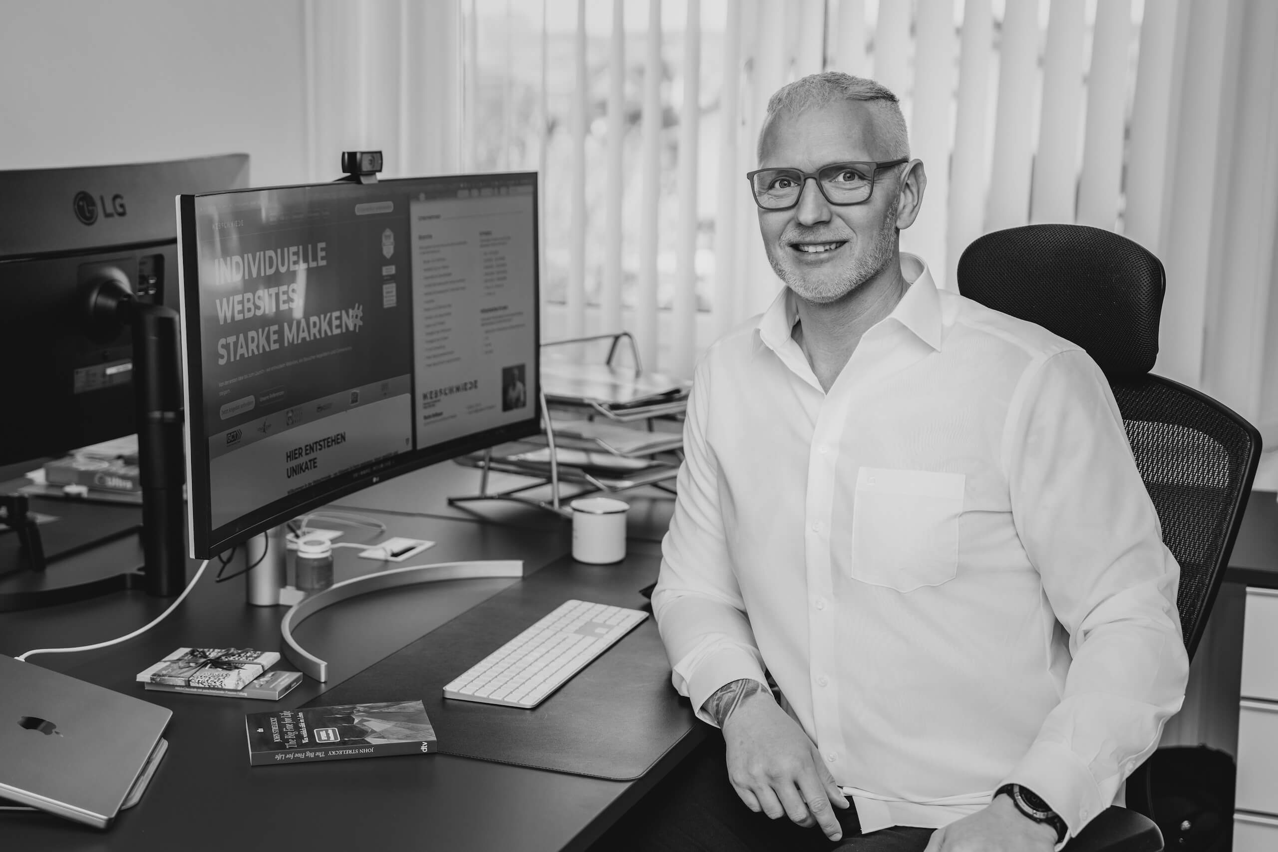 Mitarbeiter der Webschmiede arbeitet an WordPress-Website im modernen Büro, Monitor zeigt „Individuelle Websites, starke Marken“.