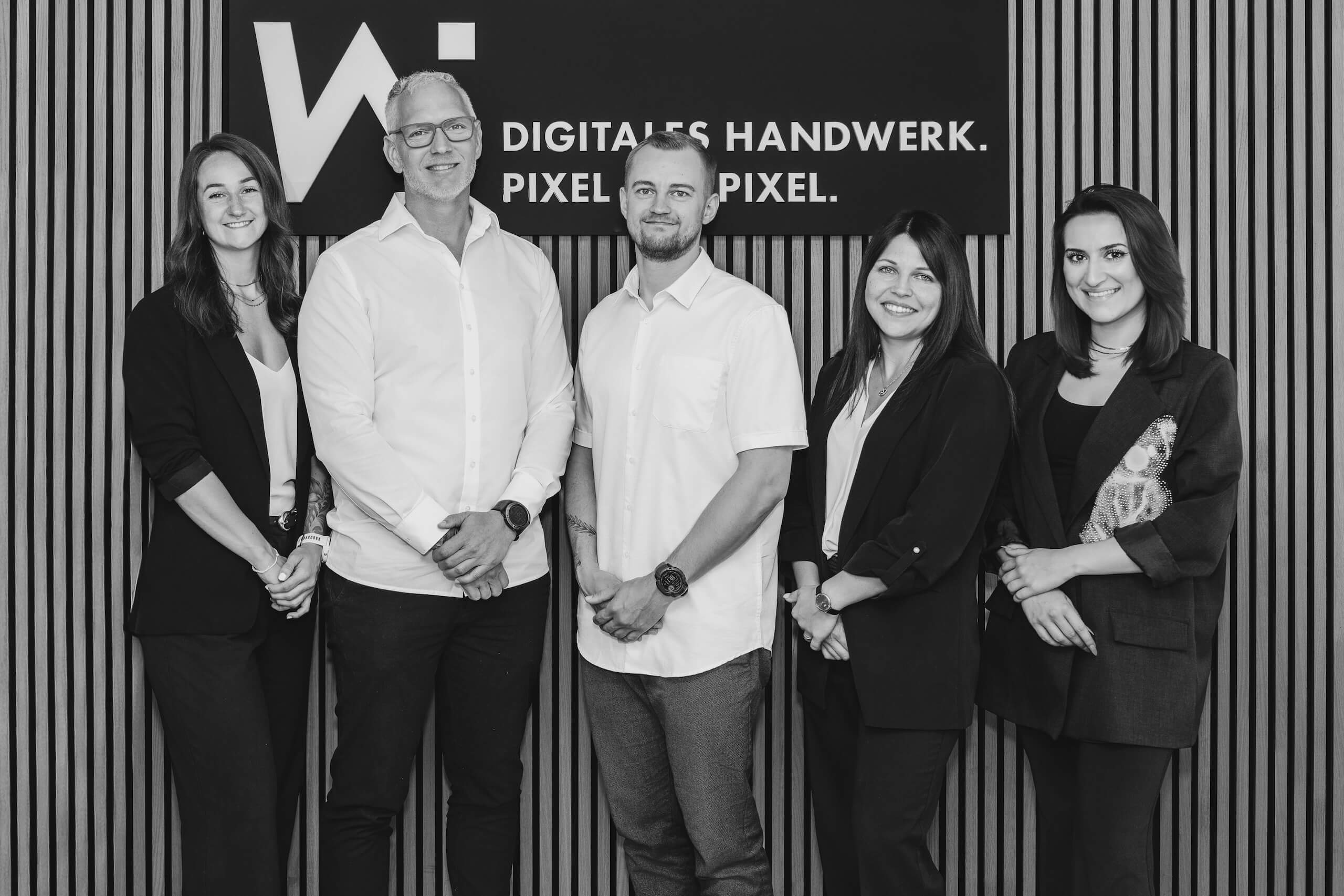 Team der Webschmiede WordPress Agentur Oberwart vor einer Tafel mit dem Slogan „Digitales Handwerk. Pixel für Pixel.“
