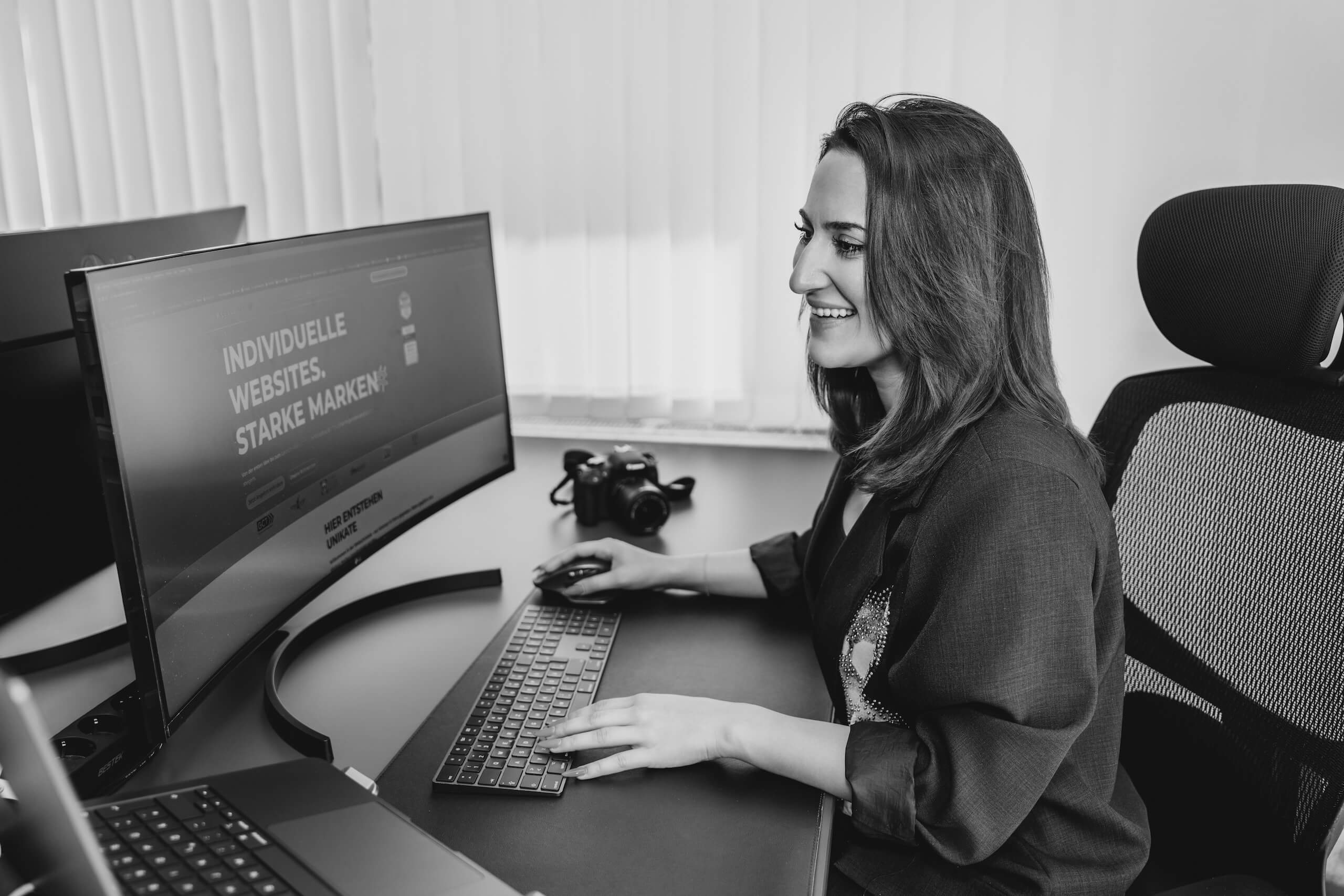 Eine Person arbeitet lächelnd an einem modernen Computer an einer WordPress-Website in einem Büro.