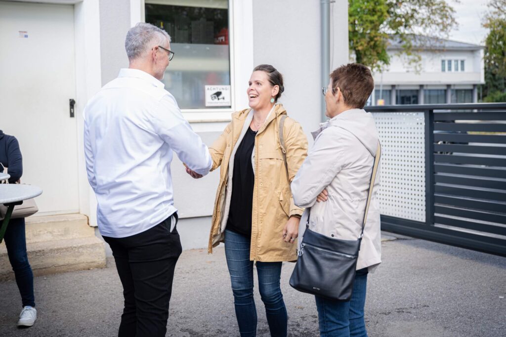 Drei Personen begrüßen sich freundlich vor einem Bürogebäude, unterstreicht die Zusammenarbeit bei Webprojekten der Webschmiede-Agentur.
