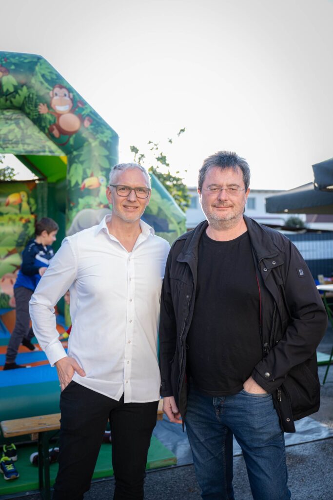 Zwei Personen vor einer Hüpfburg im Freien, lächelnd für die Kamera bei einem Event der Webschmiede WordPress Agentur.