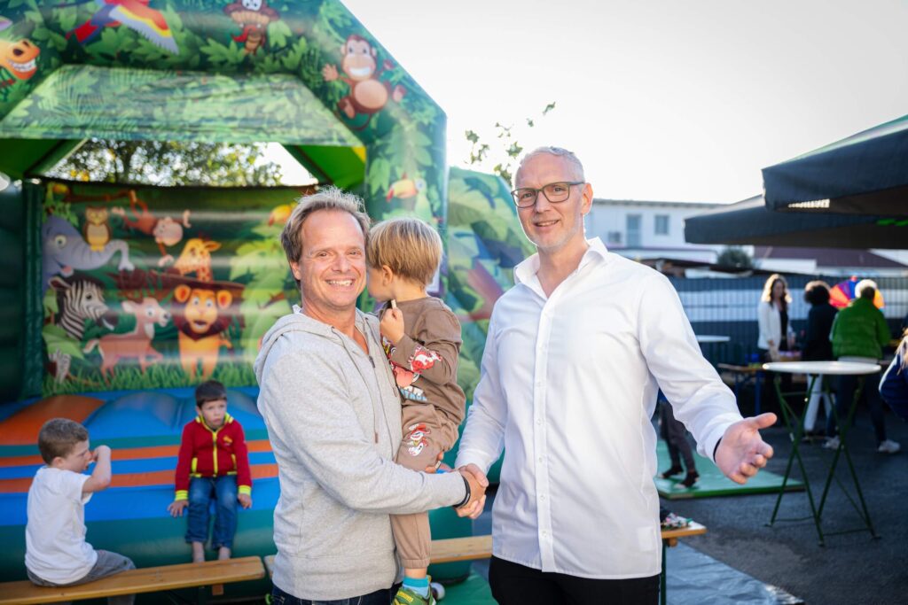Personen auf Firmenfeier vor bunter Hüpfburg, Kinder spielen fröhlich; Outdoor-Event der Webschmiede in Oberwart.